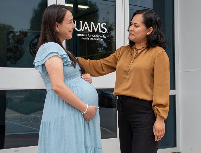 A pregnant UAMS patient stands in front of a UAMS facility talking with a doula