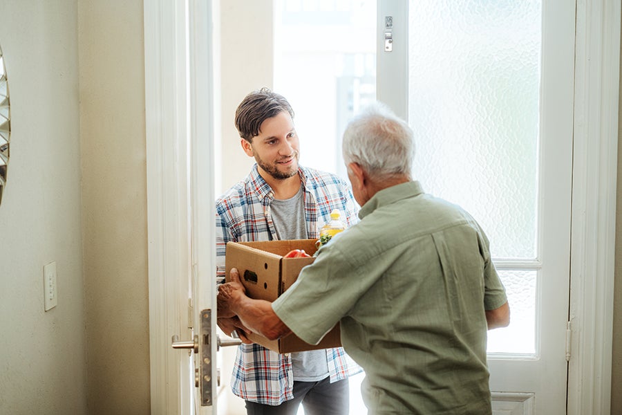 A young man delivers groceries to his elderly neighbor