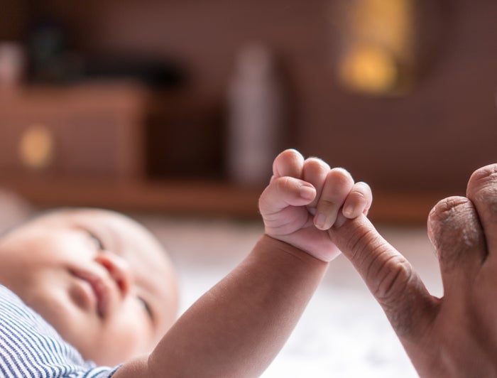 An infant holding hands with a parent