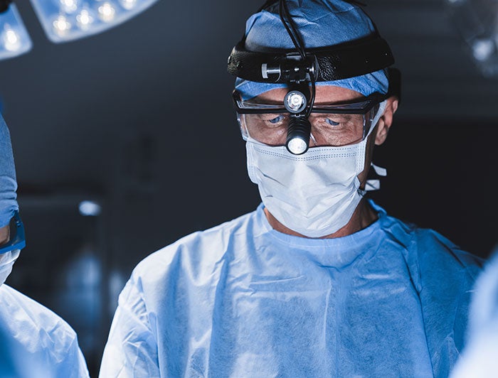 surgeon wearing scrubs and head lamp/scope operating on patient