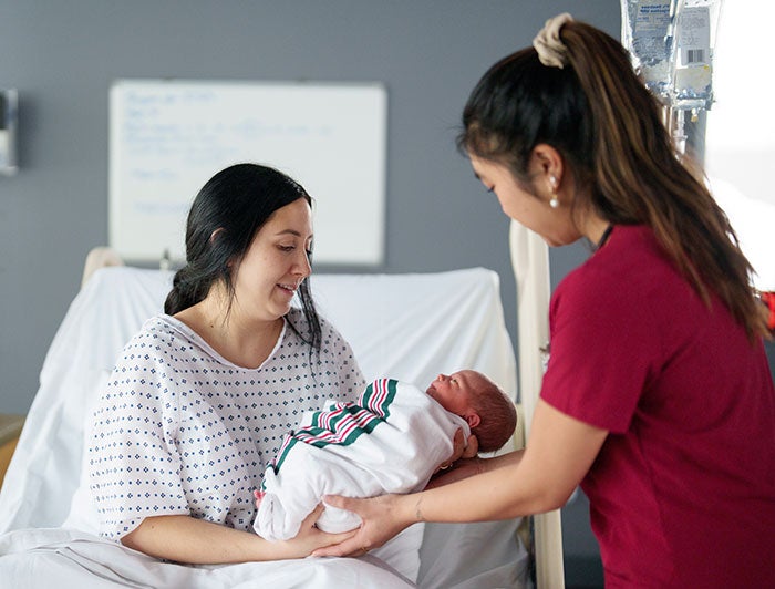 A nurse hands a newborn to mother in hospital bed