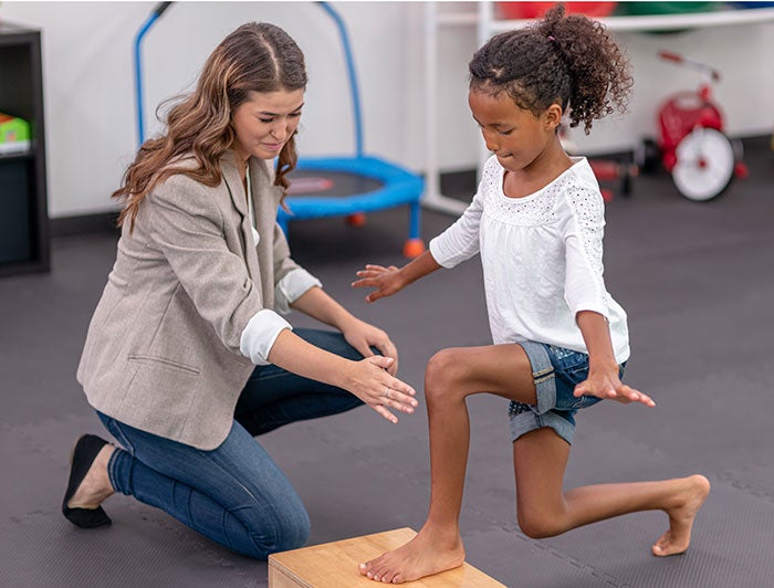 a physical therapist helps a young girl with balance exercise