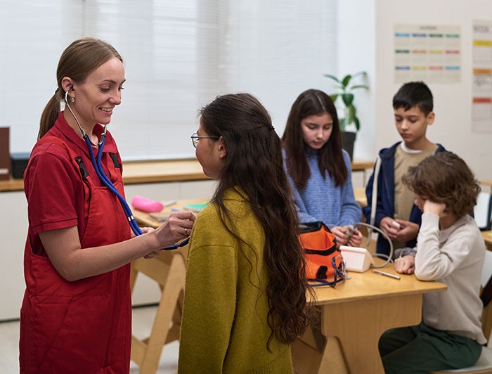 nurse giving in-classroom demonstration of stethoscope and blood pressure monitor to elementary school children