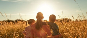 National Rural Health Day Maternal, Child Image -- a mother sitting in a field with two children watching the sun set.