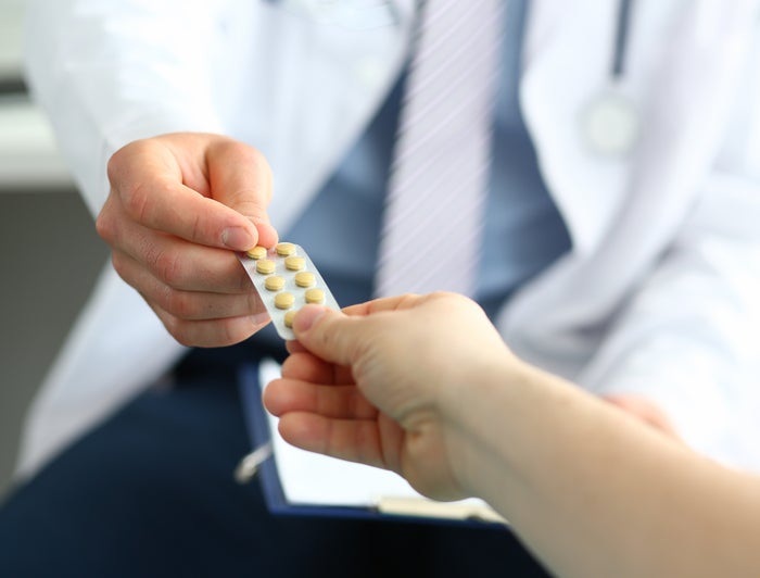 white-coated professional passing a pill pack to an outstretched hand
