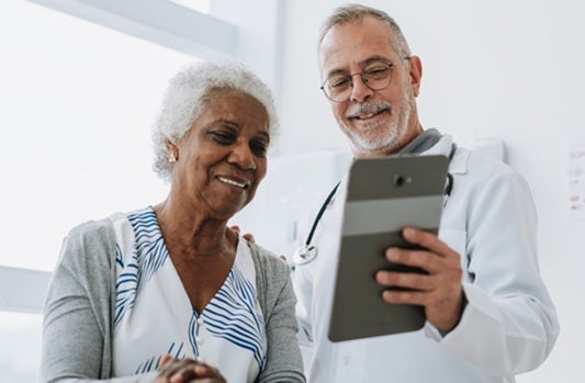an older male physician shows an elderly female patient a tablet computer