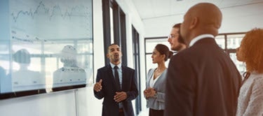 National Rural Health Day Governance Image - A group of executive standing looking at a presentation being given on a white board.