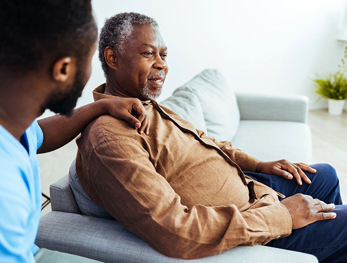A health worker talks to an elderly man sitting on a sofa