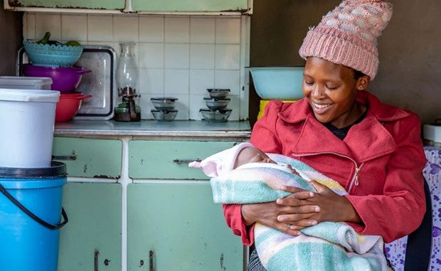 AWS’ Latest Accelerator Aims to Give a Boost to Health-Equity Startups. A seated black mother in a winter coat and hat holds her baby who is wrapped in a blanket.