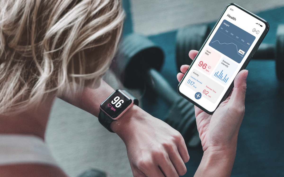 Hospitals Advance AI-Enabled Prevention at Scale. A woman in a gym compares her heart rate on her watch with the health information on her mobile phone health app.