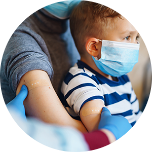 A boy sitting on his mother's lap while a clinician gives him a shot.