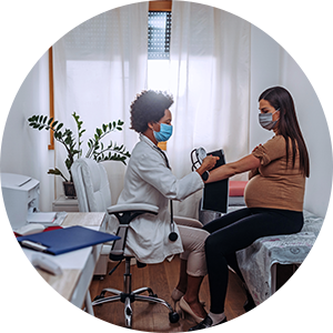 A clinician is taking a pregnant woman's blood pressure in an examination room.