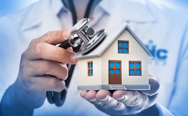 What’s Next for Unitedhealth and Optum after $5.4 Billion Acquisition of Home Care Provider? A clinician with a stethoscope held in his right hand placing the diaphragm of the stethoscope on the roof of a small house he is holding in his left hand.