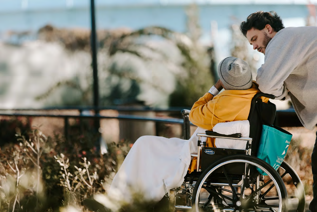 Person in a wheelchair and their escort standing behind them in an outdoor environment.