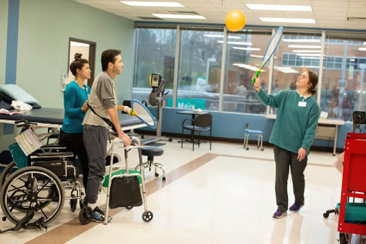 Therapist and Patient using tennis rackets to bat a yellow ball to each other during a patient therapy activity in the facility.