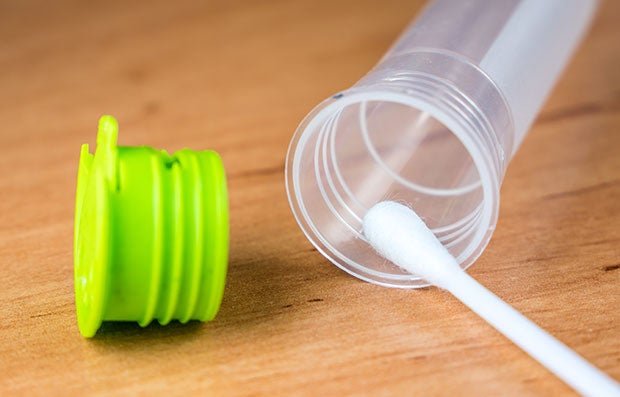 Consumers Buy into Genetic Testing Kits. A swab is placing a DNA sample in an open vial from a Genetic Testing Kit with the green vial cap next to it.