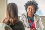 AHA Market Scan Team-Based Care Can Add Value, Improve Outcomes in Pandemic Response. A seated female clinician talks with a seated patient.