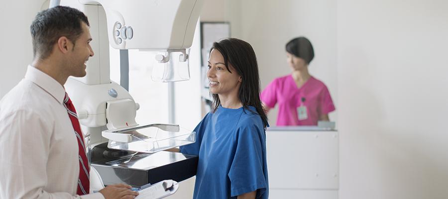 Woman in hospital gown smiling at physician holding chart