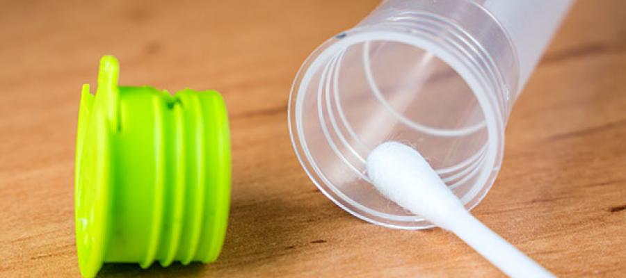 Consumers Buy into Genetic Testing Kits. A swab is placing a DNA sample in an open vial from a Genetic Testing Kit with the green vial cap next to it.