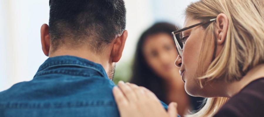 Stock photo of woman speaking to man with a comforting hand on his shoulder 