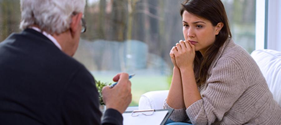 Young woman seated on a sofa speaks to a professional with a clipboard