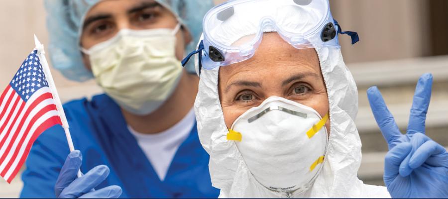 Two health workers in PPE - one holds mini American flag, the other holds up peace or victory sign
