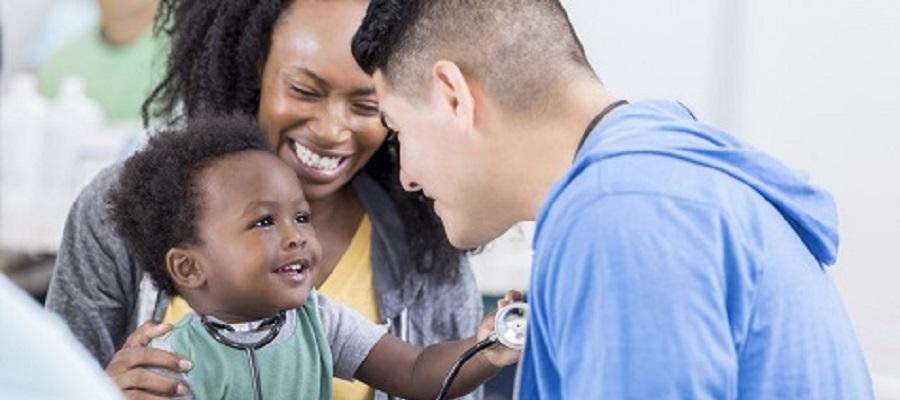 A black mother and child meet with a clinician. The child is holding the clinician's stethoscope.