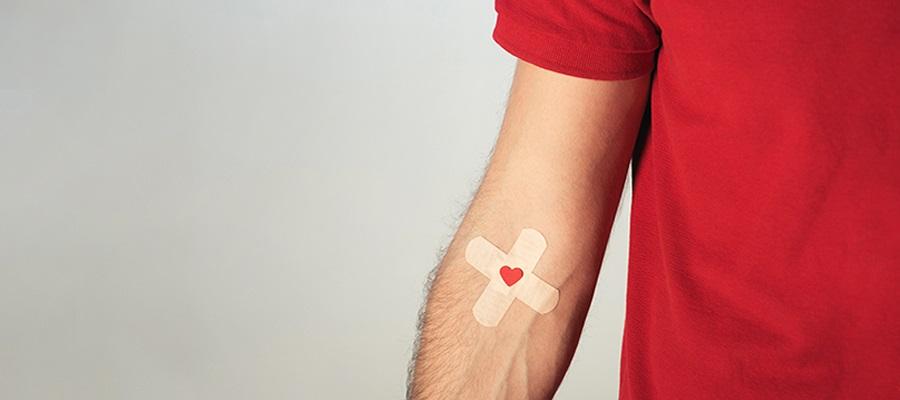 HHS campaign encourages blood donation. A man in a red T-shirt holds out his left arm which had two Band-Aids in the shape of a cross with a heart in the middle attached to the inside of his elbow after making a blood donation.