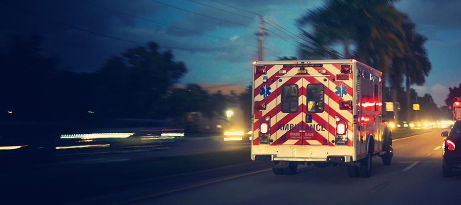 The Next Wave of Emergency Preparedness in Health Care. An ambulance driving toward a hospital viewed from behind.