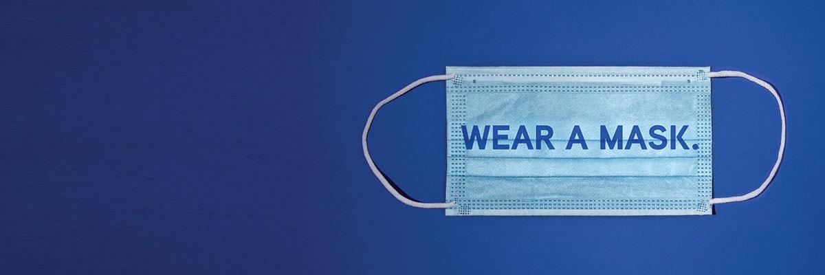 Phrase "Wear A Mask." imposed over a surgical face mask on a blue background.