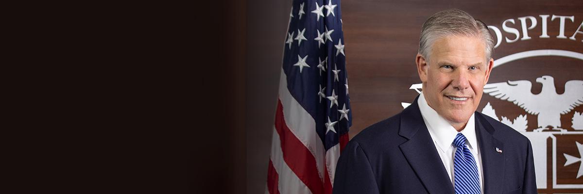 Rick Pollack, American Hospital Association CEO and President standing in front of United States flag and the AHA seal.