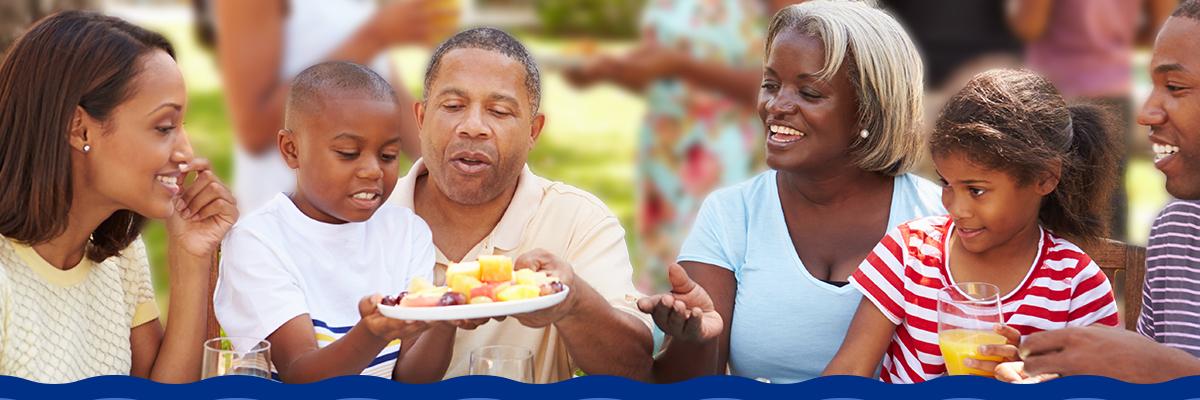 Black family including a woman, man, boy, girl and an older woman pass a plate of food at a barbecue