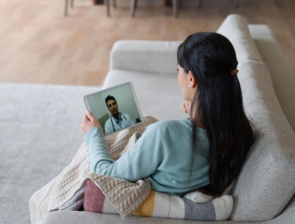 Woman seated on a sofa views a webinar speaker on a tablet