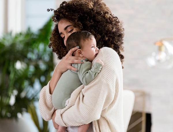 Stock image of a young curly-haired mother holding an infant against her shoulder
