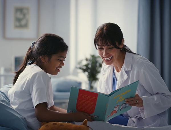 A woman reads a book to a smiling girl