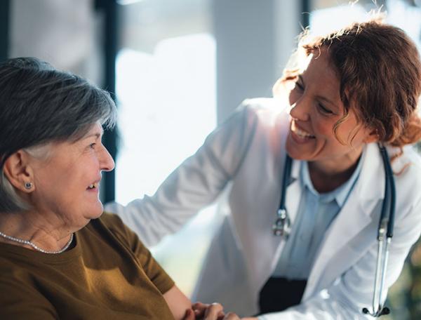 A female doctor smiles at an older woman she is assisting