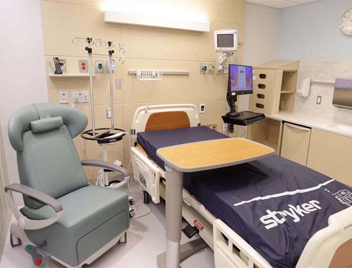 A small hospital room set up with a stryker hospital bed and a side chair