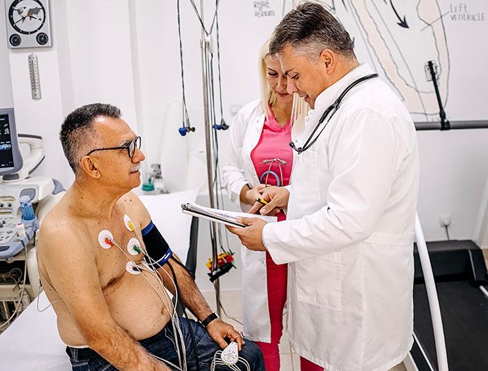 Cedars Sinai. Clinicians in white coats review notes next to a patient wearing EKG leads and BP cuff.