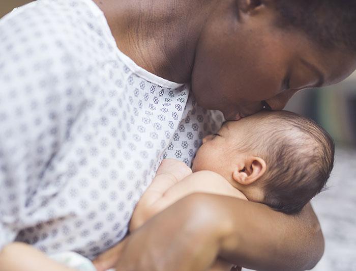 stock image of a mother in hospital gown kissing her newborn on the head