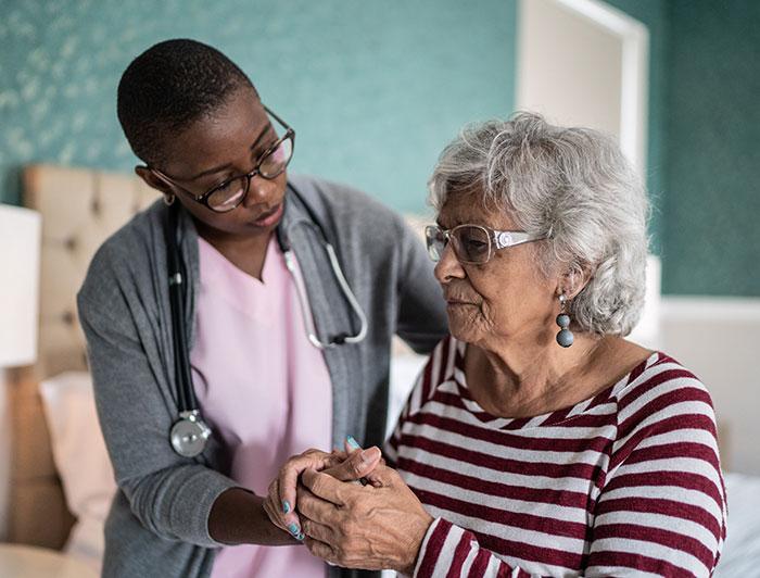 A female clinician sits in a residential setting with an elderly woman.