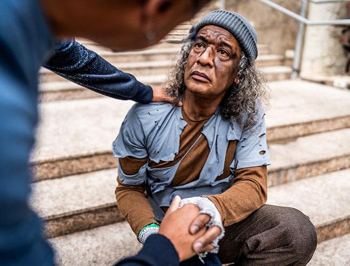 A homeless man sits on steps outside a building, listening to a person doing community outreach