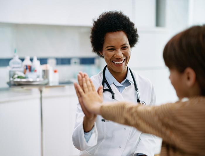 A female physician high fives a young patient in an exam room
