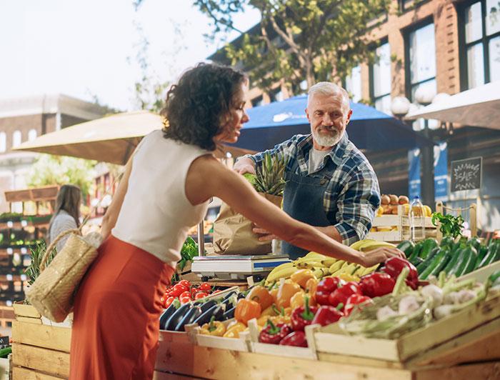 A woman checks fresh produce at an outdoor market as the vendor looks on