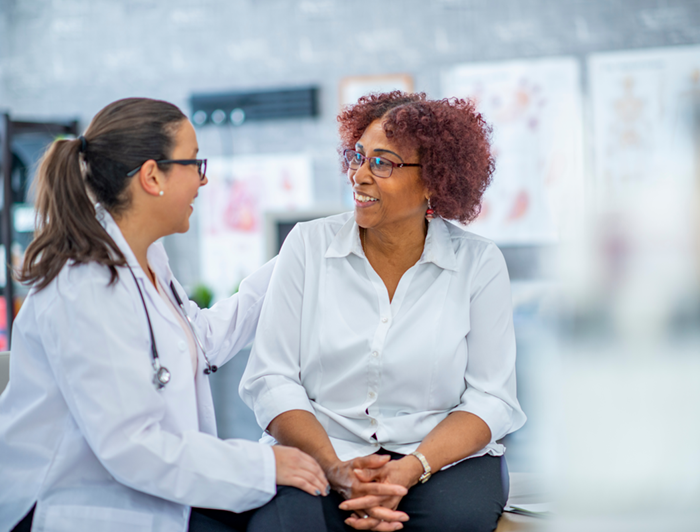 A middle aged woman sits talking with a female physician