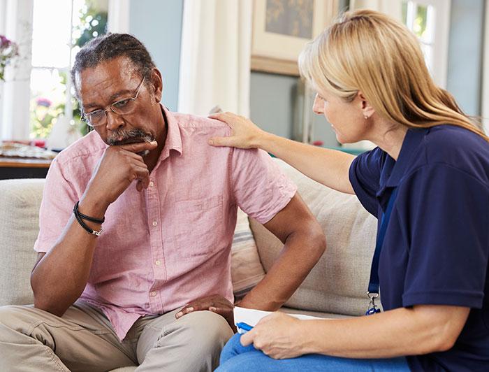An older man sits talking with a female carer