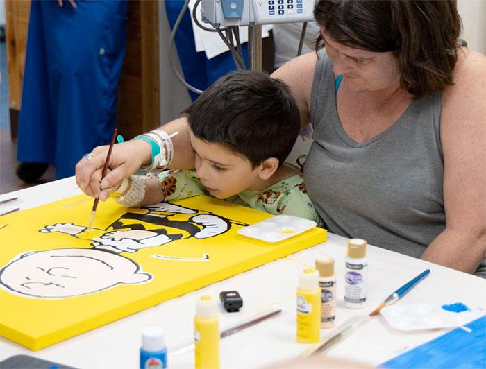 A young patient and carer paint a Charlie Brown canvas together