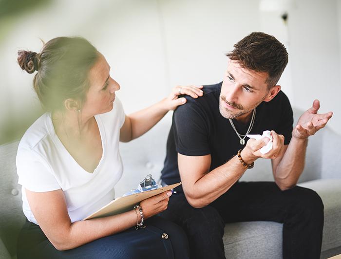Woman holding clipboard talks with man holding tissues