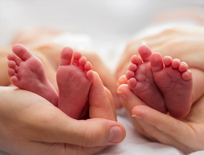 tiny infants' lay side-by-side, their feet cradled in carer's hands