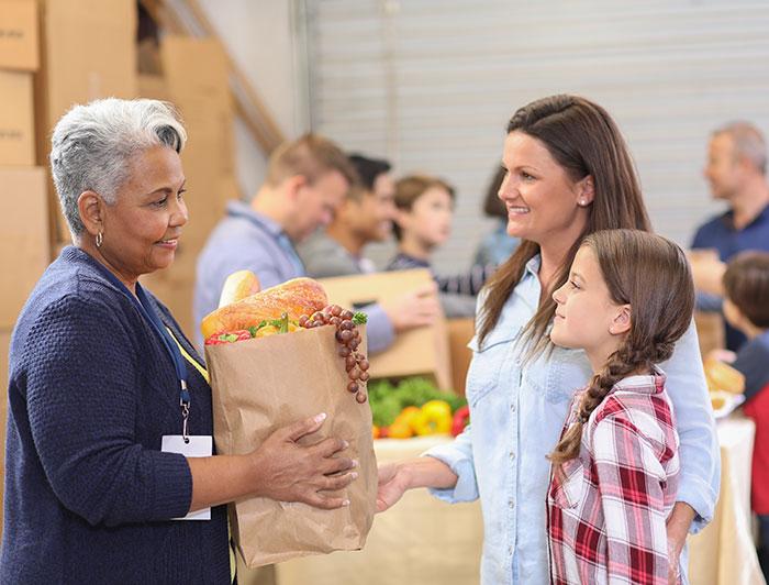 An older woman volunteer giving a bag of groceries to a woman and child