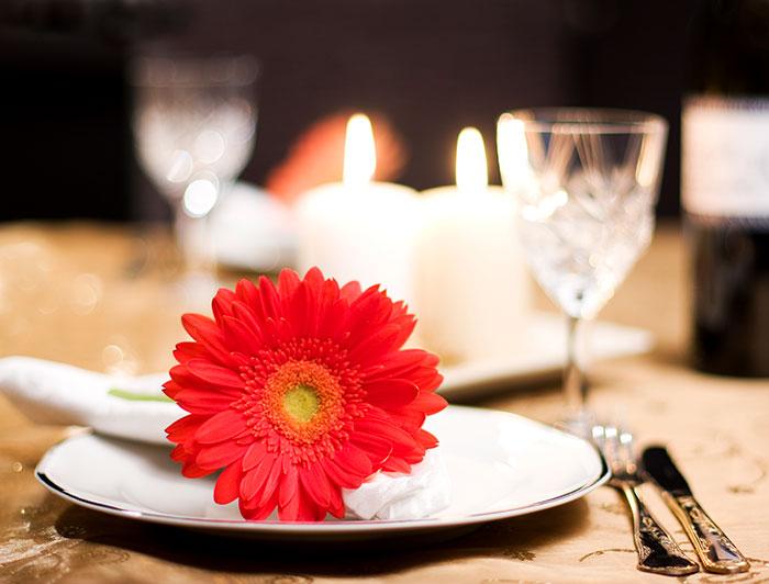a gerbera daisy rests on a plate as part of a romantic, candle-lit table